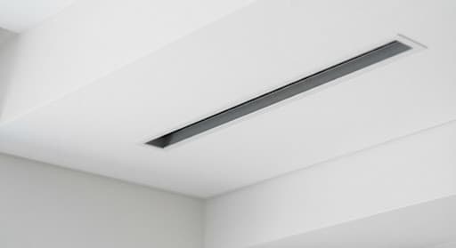 Close up architectural detail of modern minimalist recessed ceiling aircon slot in a pristine white interior with subtle shadow gaps and immaculate dry condition, no water stains
